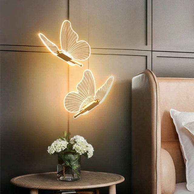 Butterfly-shaped wall lights on a wall with a vase of flowers on a table.